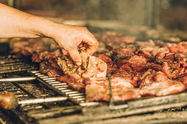 Nierozpoznany szef kuchni gotuje kawałki mięsa na grillu i używa rąk.