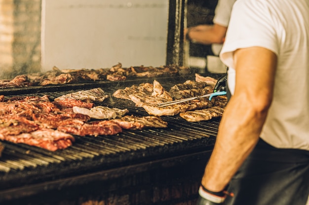 Nierozpoznany Szef Kuchni W Rękawiczkach Gotuje Stek Na Grillu I Używa Szczypiec Do Mięsa.