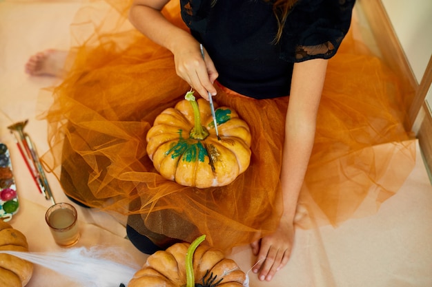 Nierozpoznawalna dziewczyna dekorująca pomarańczową dynię, rysująca twarz Jack-O-Lantern na Halloween