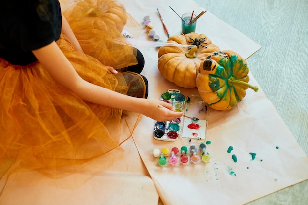 Nierozpoznawalna dziewczyna dekorująca pomarańczową dynię rysunkową twarz JackOLantern na Halloween