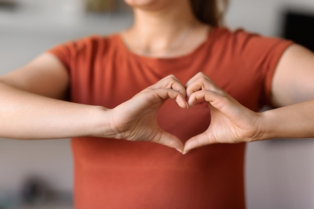 Nierozpoznawalna kobieta robi gest serca rękami w pobliżu klatki piersiowej