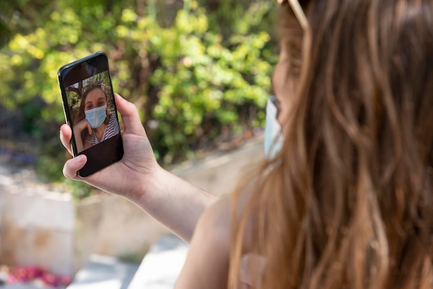 Zdjęcie nierozpoznawalna kobieta z maską na twarz używa smartfona do robienia selfie – zdjęcie stockowe