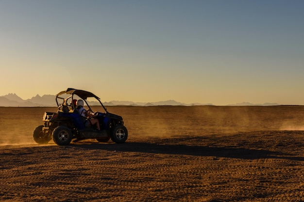 Nierozpoznawalni ludzie jeżdżący buggy podczas safari o zachodzie słońca na arabskiej pustyni niedaleko miasta Hurghada w Egipcie