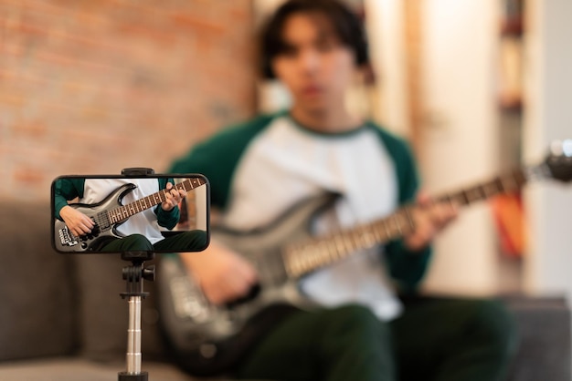 Nierozpoznawalny koreański facet grający na gitarze elektrycznej, filmujący na smartfonie w pomieszczeniu