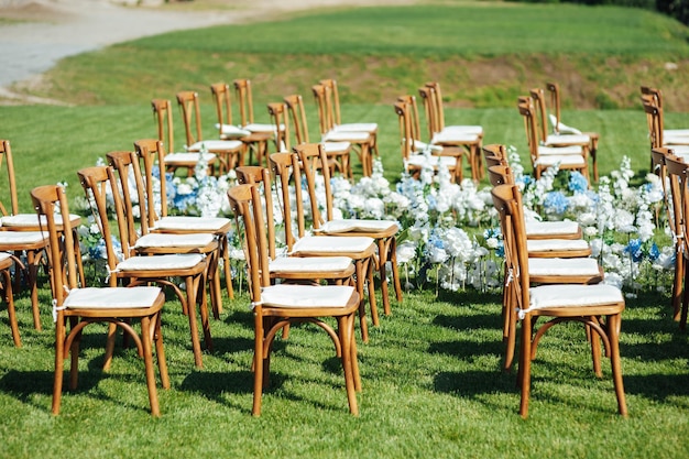 Niesamowicie piękna ceremonia plenerowa na zielonej trawie i drewnianych krzesłach oraz w dniu ślubu ze świeżymi kwiatami