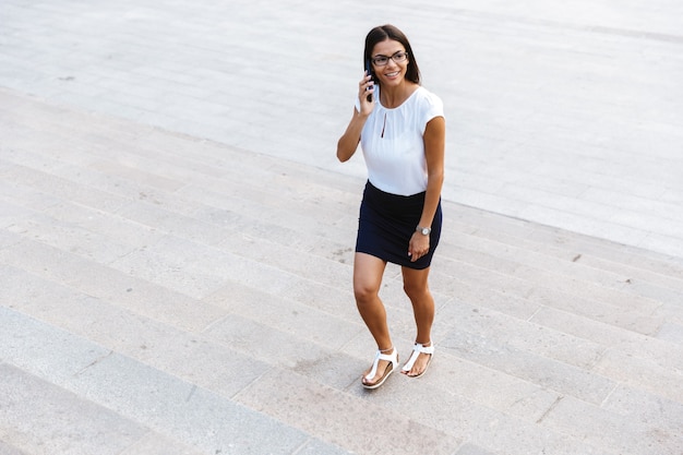 Niesamowita ładna biznesowa kobieta spaceru na zewnątrz, rozmawiając przez telefon komórkowy