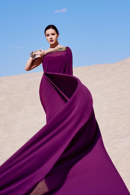 Niesamowita piękna brunetka z pawim piórem w fioletowej tkaninie na pustyni