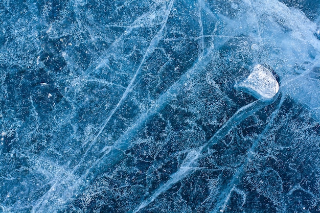 Niesamowita struktura lodu z pęknięciami i pęcherzykami powietrza. Mała stopiona kry na niebieskim lodzie. Zimowy wzór. Poziomy.