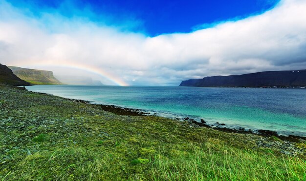 Niesamowity letni krajobraz z błękitnym morzem, białymi chmurami i tęczą. Islandia, Europa