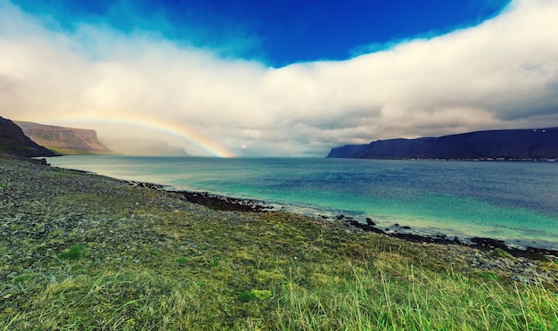 Niesamowity letni krajobraz z błękitnym morzem, białymi chmurami i tęczą Islandia Europa