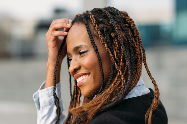 Nieśmiała Afroamerykanka. Szczęśliwy model uśmiech. Młoda czarna kobieta uśmiechnięta w selektywnej ostrości na zewnątrz, fryzura moda, koncepcja szczęścia
