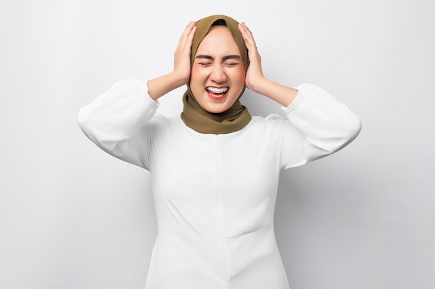 Niespokojna młoda azjatycka muzułmanka nosząca hidżab trzymająca rękę na głowie i wyglądająca na zmartwioną odizolowaną na białym tle Koncepcja religijnego stylu życia ludzi