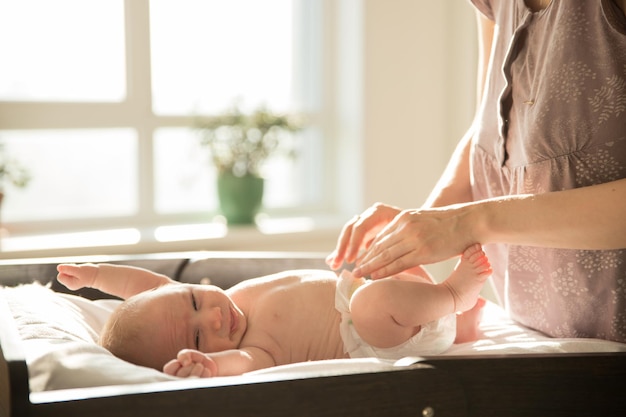 Niespokojne dziecko leżące na łóżeczku i stojąca nad nim mama