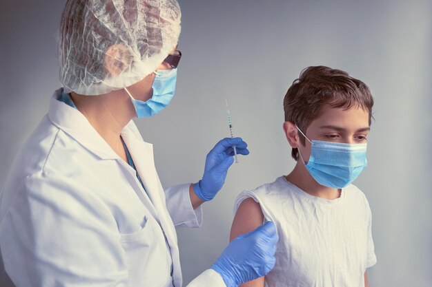 Niespokojny dzieciak robi twarz przestraszony strzykawki lekarz medyk pielęgniarka lekarz w białej sukni i masce na twarz szczepi nastoletniego chłopca nowa normalna koncepcja obie osoby noszące maski na twarz