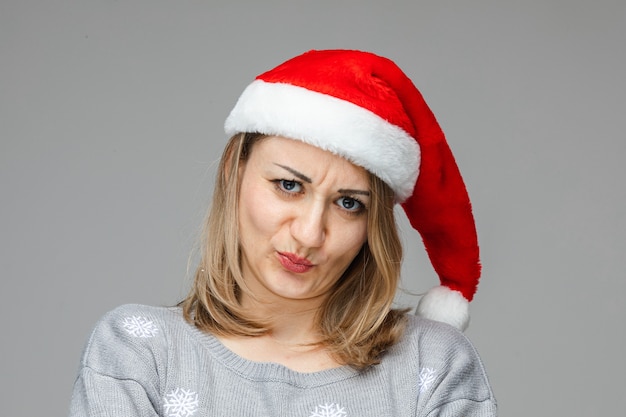 Nieszczęśliwa kobieta w czerwono-białym świątecznym kapeluszu, niezadowolona z zaciśniętymi ustami. Koncepcja nowego roku