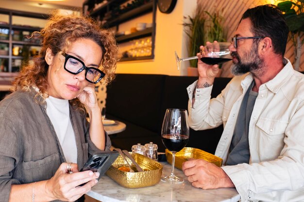 Zdjęcie nieszczęśliwa para ignorująca się w restauracji, patrząca na telefon komórkowy, gniewna para małżeńska obiadująca w kawiarni.
