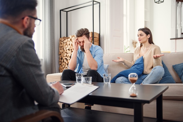Nieszczęśliwa para kłócąca się, walcząca, nieporozumienia w biurze psychologów, sfrustrowana młoda rodzina dyskutująca o problemach w relacjach ze swoim terapeutą