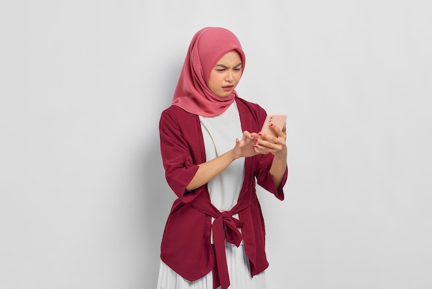 Nieszczęśliwa piękna Azjatycka kobieta w luźnej koszuli przy użyciu telefonu komórkowego reagującego na złe wieści odizolowane na białym tle