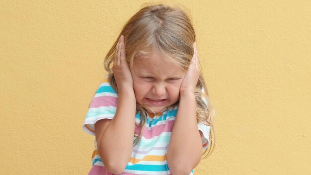 Zdjęcie nieszczęśliwa, smutna, wściekła dziewczynka zamyka oczy i zakrywa uszy rękami, denerwowana głośnym hałasem.