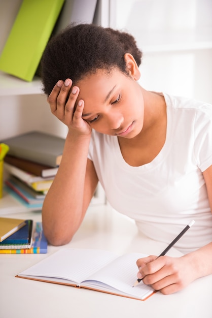 Nieszczęśliwa uczennica siedzi przy stole i pisze pracę domową.