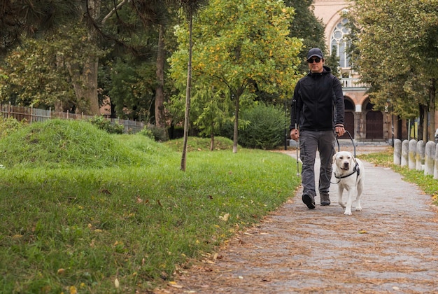 Niewidomy człowiek idący z pomocą psa przewodnika przez park jesienny