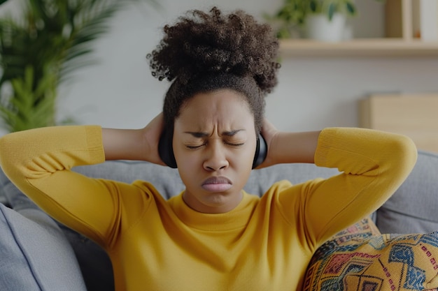 Niezadowolona i wściekła młoda afroamerykańska kobieta siedząca w domu na kanapie i zakrywająca uszy przed nadmiernym hałasem