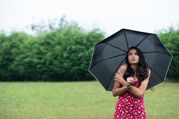 Niezadowolona młoda latynoska kobieta marznąca pod parasolem w naturze