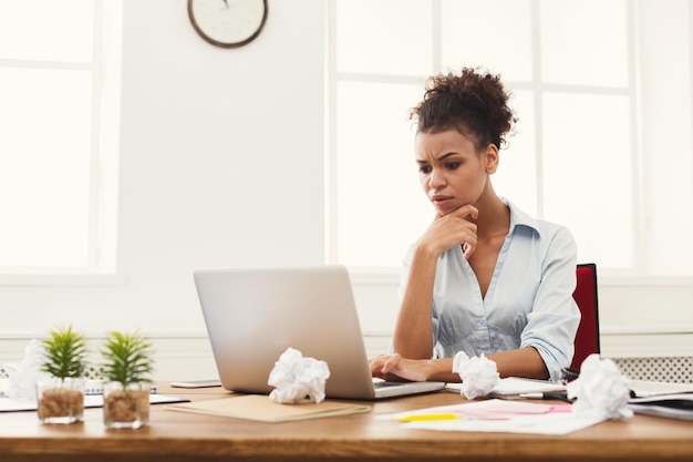 Niezadowolony biznes afro-amerykański kobieta pracuje na laptopie w biurze. Kobieta wpisuje coś na komputerze, siedząc w swoim miejscu pracy, skopiuj miejsce