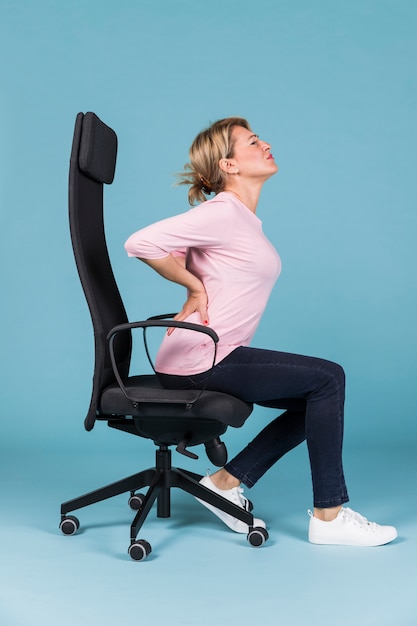 Niezadowolony kobiety obsiadanie w krześle ma backache na błękitnym tle