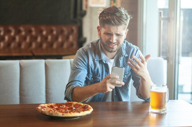 Niezadowolony mężczyzna patrzący na smartfona siedząc w kawiarni