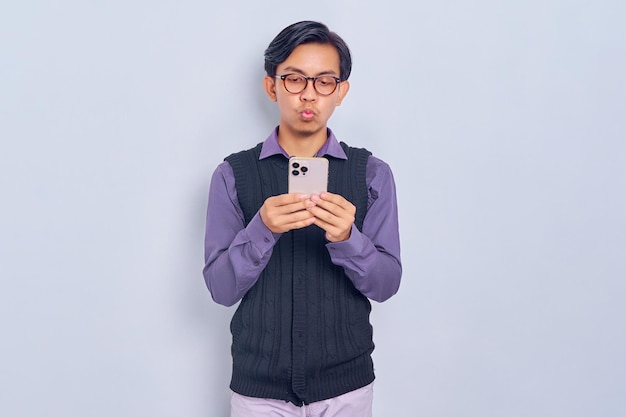 Niezadowolony młody azjatycki człowiek w casualowej koszuli i kamizelce za pomocą smartfona na białym tle Koncepcja stylu życia ludzi