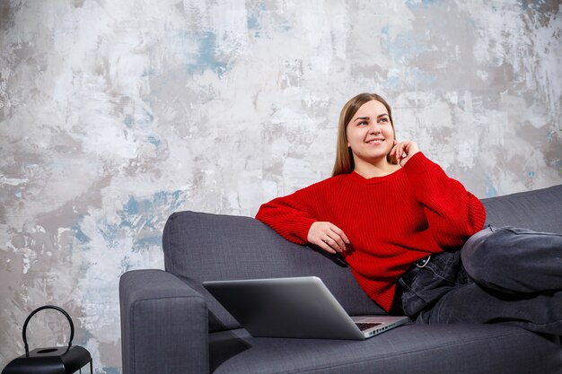 Niezależna kobieta siedzi na kanapie w przytulnym wnętrzu domu i pracuje zdalnie na nowoczesnym laptopie, doświadczona kobieta ogląda webinarium online na stronie internetowej. Praca w domu podczas kwarantanny