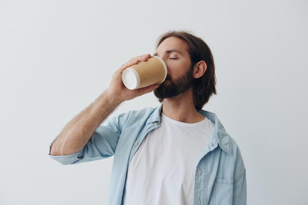 Niezależny milenijny mężczyzna z brodą pijący kawę z kubka kraba w stylowych hipsterskich ubraniach na białym tle