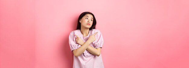 Niezdecydowana azjatycka kobieta nie może się zdecydować, wskazując palcami na boki i wyglądając na zamyśloną, dokonując wyboru st