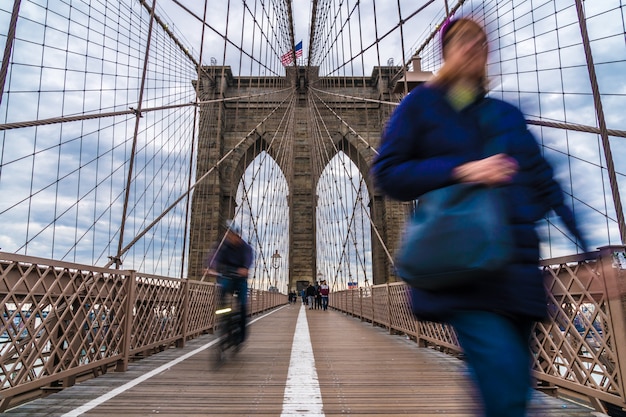 Niezdefiniowany pasażer i turysta spacerujący i jadący rowerem po moście Brooklyn.