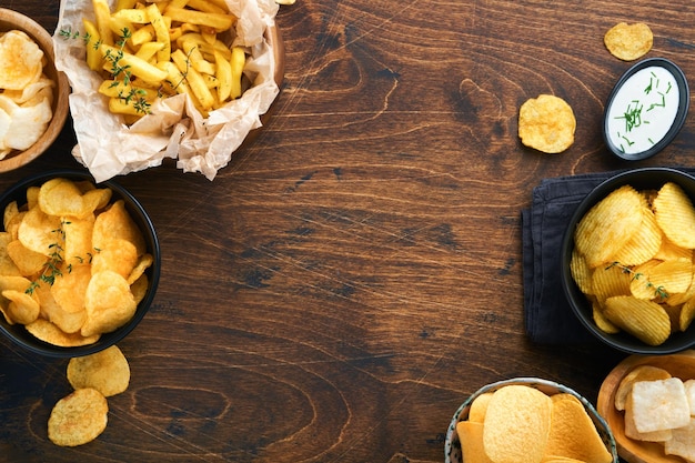 Niezdrowe jedzenie lub przekąski Wszystkie klasyczne przekąski ziemniaczane z orzeszkami ziemnymi, popcornem i krążkami cebuli oraz solonymi precelkami w talerzach misek na starym drewnianym tle Niezdrowe jedzenie dla zębów skóry serca