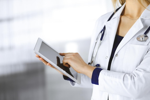 Nieznana kobieta-lekarz trzyma w rękach komputer tablet, stojąc w szafce klinicznej. Kobieta lekarz w pracy, zbliżenie. Doskonała usługa medyczna w szpitalu. Koncepcja medycyny.