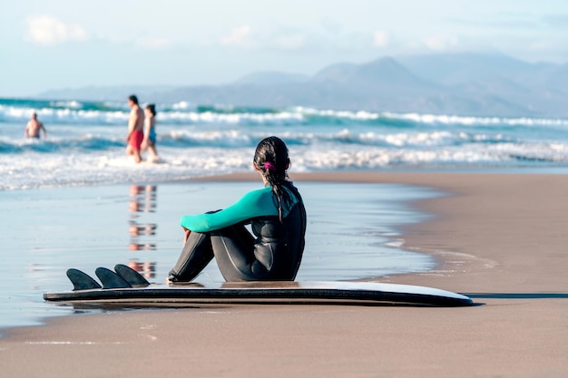 nieznana surferka siedząca samotnie na plaży z deską surfingową obserwująca horyzont