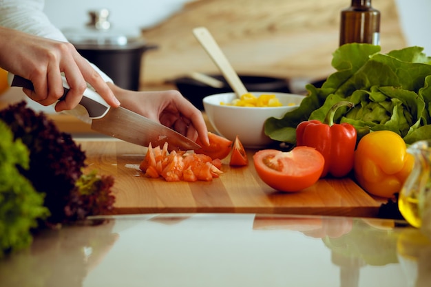 Nieznane ludzkie ręce, gotowanie w kuchni. Kobieta kroi czerwone pomidory. Zdrowy posiłek i wegetariańska koncepcja żywności.