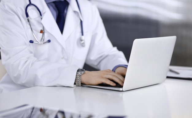Nieznany lekarz mężczyzna siedzi i pracuje z laptopem w klinice w swoim miejscu pracy, zbliżenie. Młody lekarz w pracy. Doskonała usługa medyczna, koncepcja medycyny.