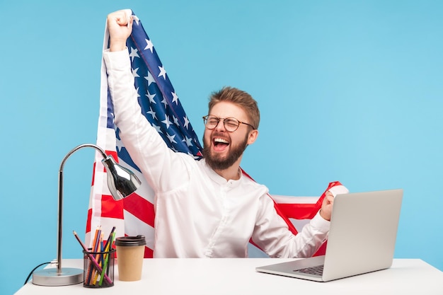 Niezwykle szczęśliwy biznesmen podnoszący amerykańską flagę i szaleńczo krzyczący z radości w biurze, świętujący Święto Pracy lub Dzień Niepodległości USA 4 lipca, rządowe wsparcie zatrudnienia. studio strzał