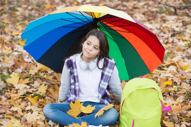 Nigdy więcej deszczu dziewczyna z plecakiem pod ochroną przed deszczem dziecko odpoczywa w jesiennym lesie jesienne liście w parku powrót do szkoły ciesz się ciepłą pogodą sezonową szczęśliwy dzieciak siedzący pod kolorowym parasolem