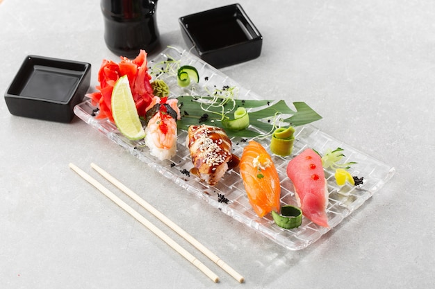 Nigiri sushi z łososiem, węgorzem, tuńczykiem i krewetkami, podawane na przezroczystym talerzu.