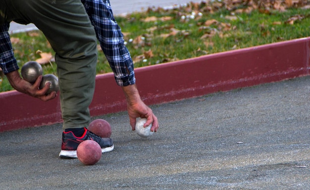 Zdjęcie niska część człowieka trzymającego piłki petanque na chodniku