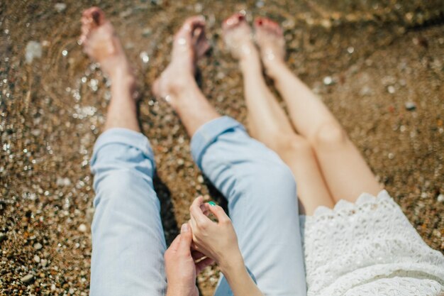 Zdjęcie niska część pary siedzącej na brzegu na plaży