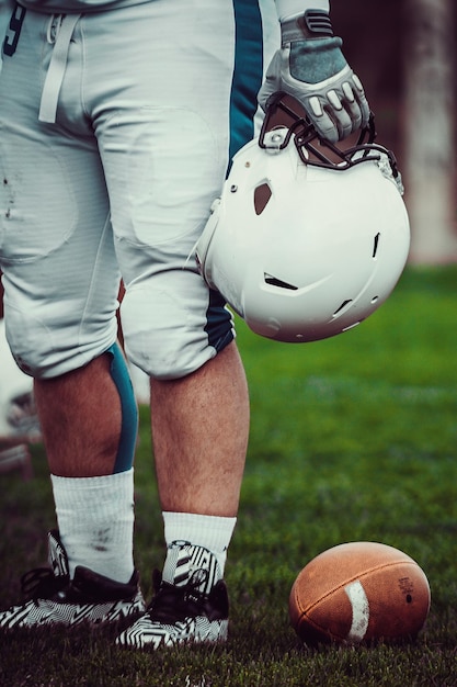 Zdjęcie niska część piłkarza amerykańskiego futbolu trzymającego hełm podczas stania na boisku