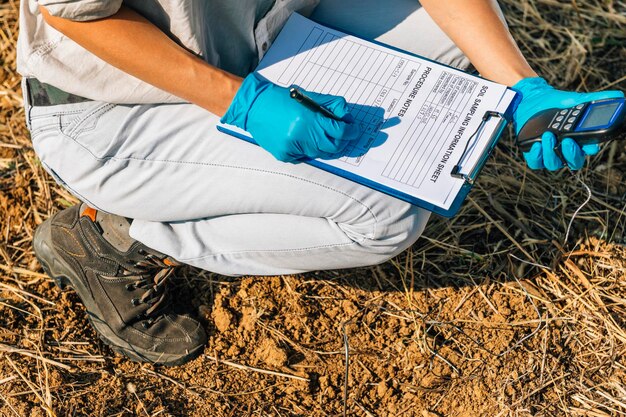 Niska sekcja agronomisty piszącego na papierze podczas przykucania się na polu