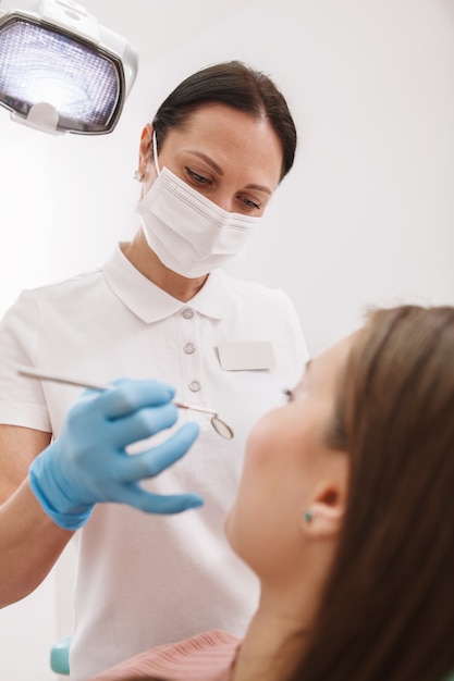 Niski kąt pionowe ujęcie profesjonalnego dentysty w masce medycznej i rękawiczkach, badającego zęby pacjenta