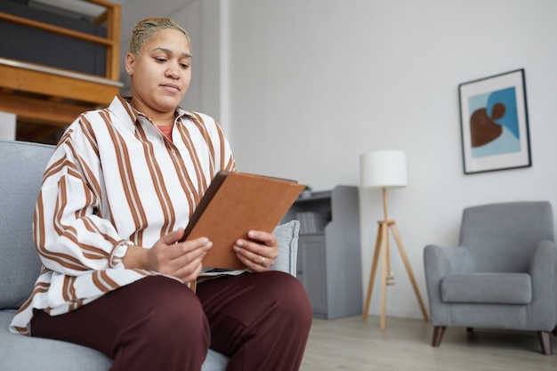 Niski kąt portret nowoczesnej kobiety rasy mieszanej trzymającej cyfrowy tablet podczas korzystania z aplikacji online w domu, skopiuj przestrzeń