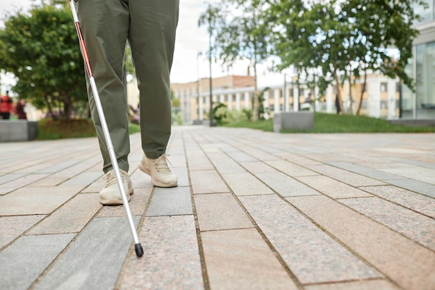 Zdjęcie niski kąt ujęcia niewidomego mężczyzny chodzącego po mieście i używającego laski na przestrzeni kopii chodnika
